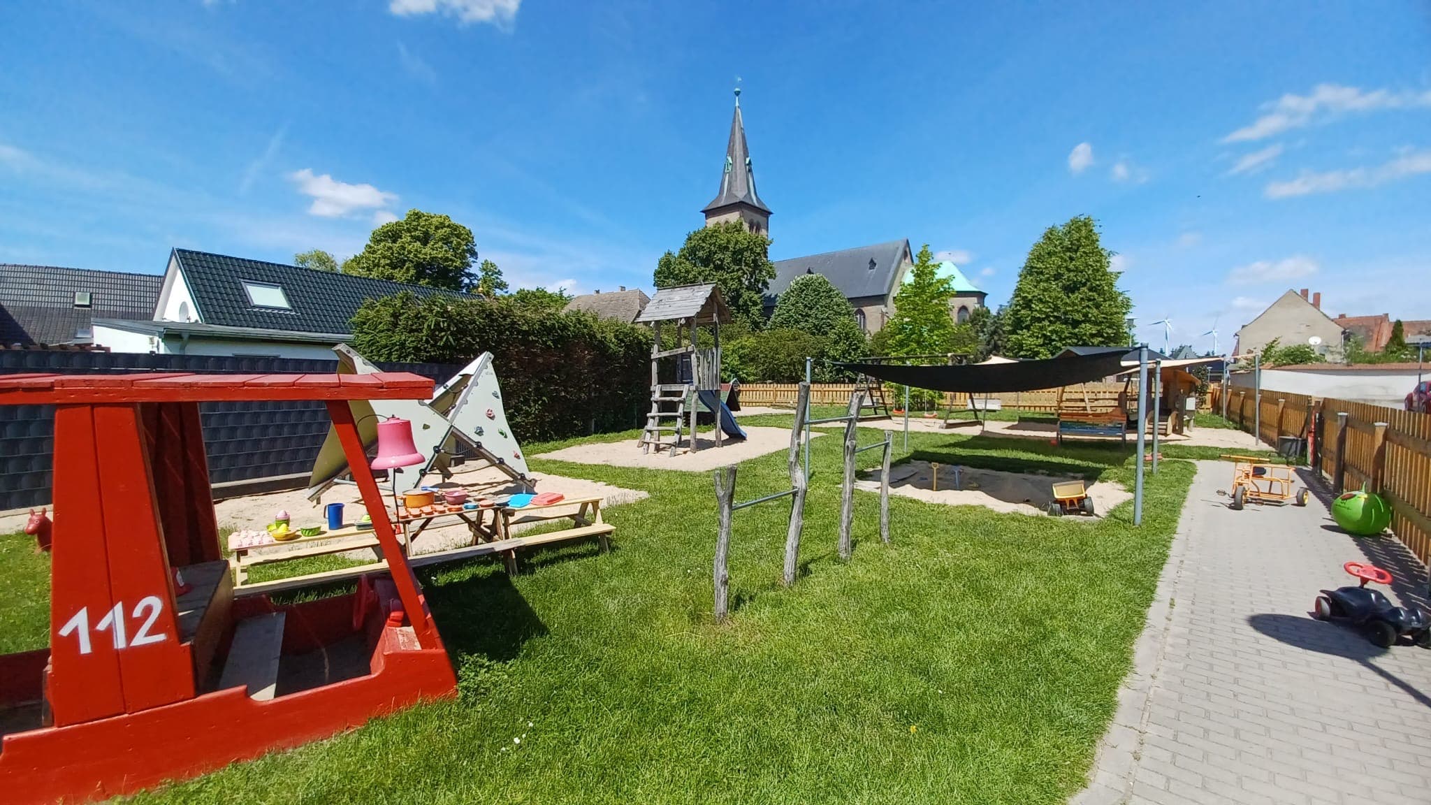 Unser Garten mit Spielgeräten und Kirchturm im Hintergrund